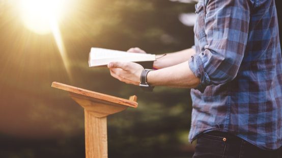 uma-tomada-de-foco-superficial-de-um-homem-lendo-biblia-em-pe-perto-de-um-podio